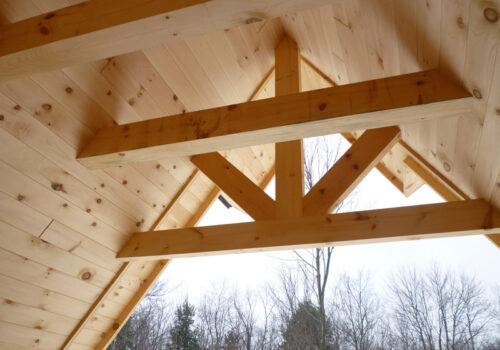 Interior view of a rustic timber frame showcasing square eastern white pine beams and natural wood paneling, emphasizing craftsmanship and structural design for residential or commercial applications.