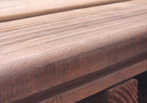 Close-up of KDAT Brown Decking showcasing rich, pre-finished wood texture with grooves for hidden fasteners, highlighting its quality and suitability for decking and framing products.