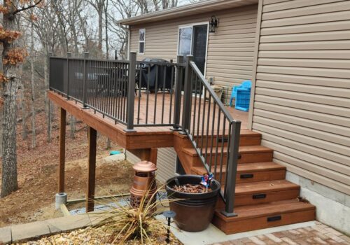 KDAT decking and railing system installed on a residential deck with steps, showcasing pre-finished brown lumber and metal railings, surrounded by a natural landscape.