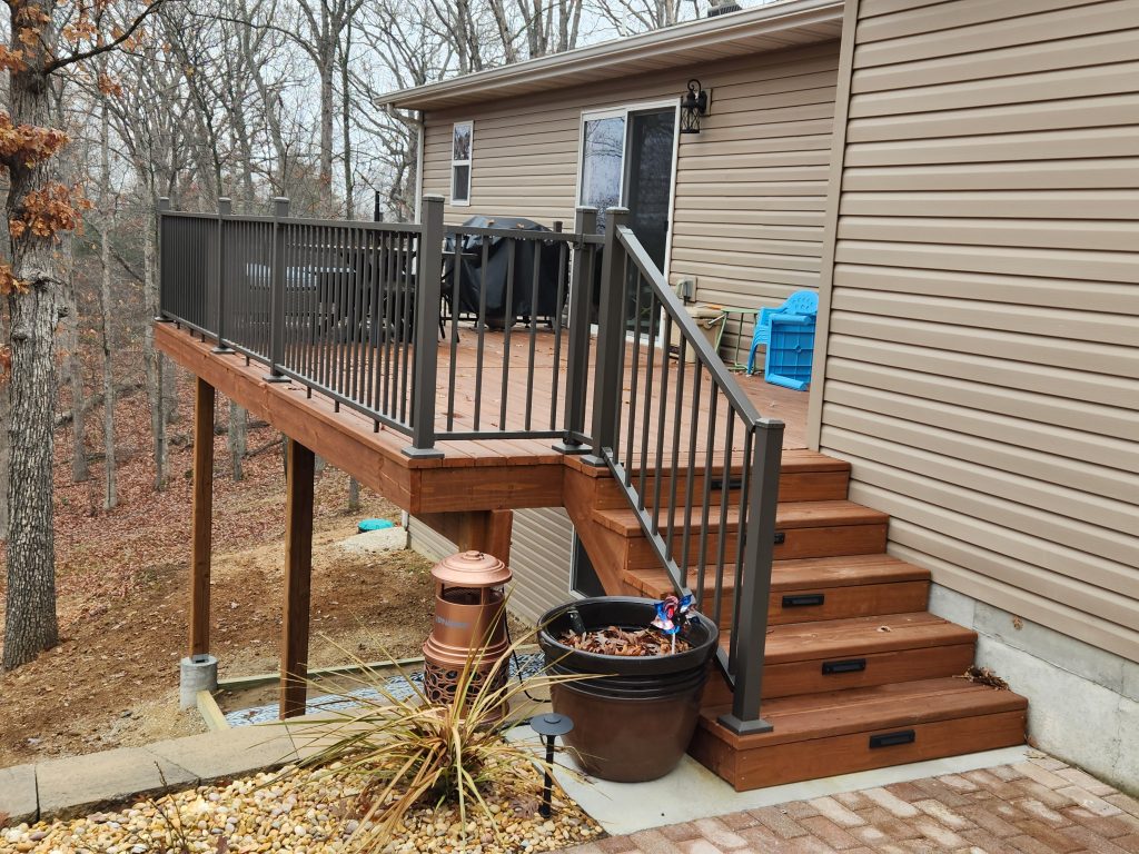 Deck with KDAT materials featuring black railing, stairs, and surrounding landscaping, illustrating stable substructure for composite and wood decking.