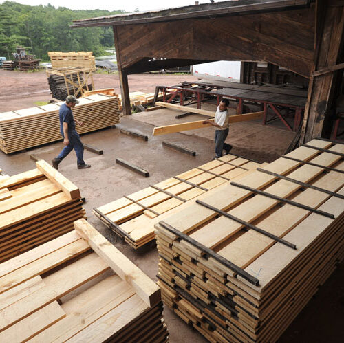 Two workers at Estemerwalt Lumber Products yard, surrounded by stacked lumber, demonstrating the full-service lumber operation in Honesdale, PA.