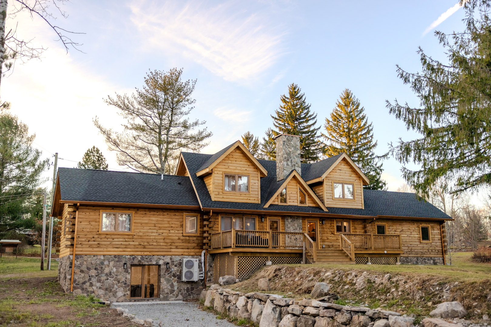 Log home exterior featuring wooden siding, stone foundation, and a large deck, surrounded by trees, illustrating design possibilities for log home construction.